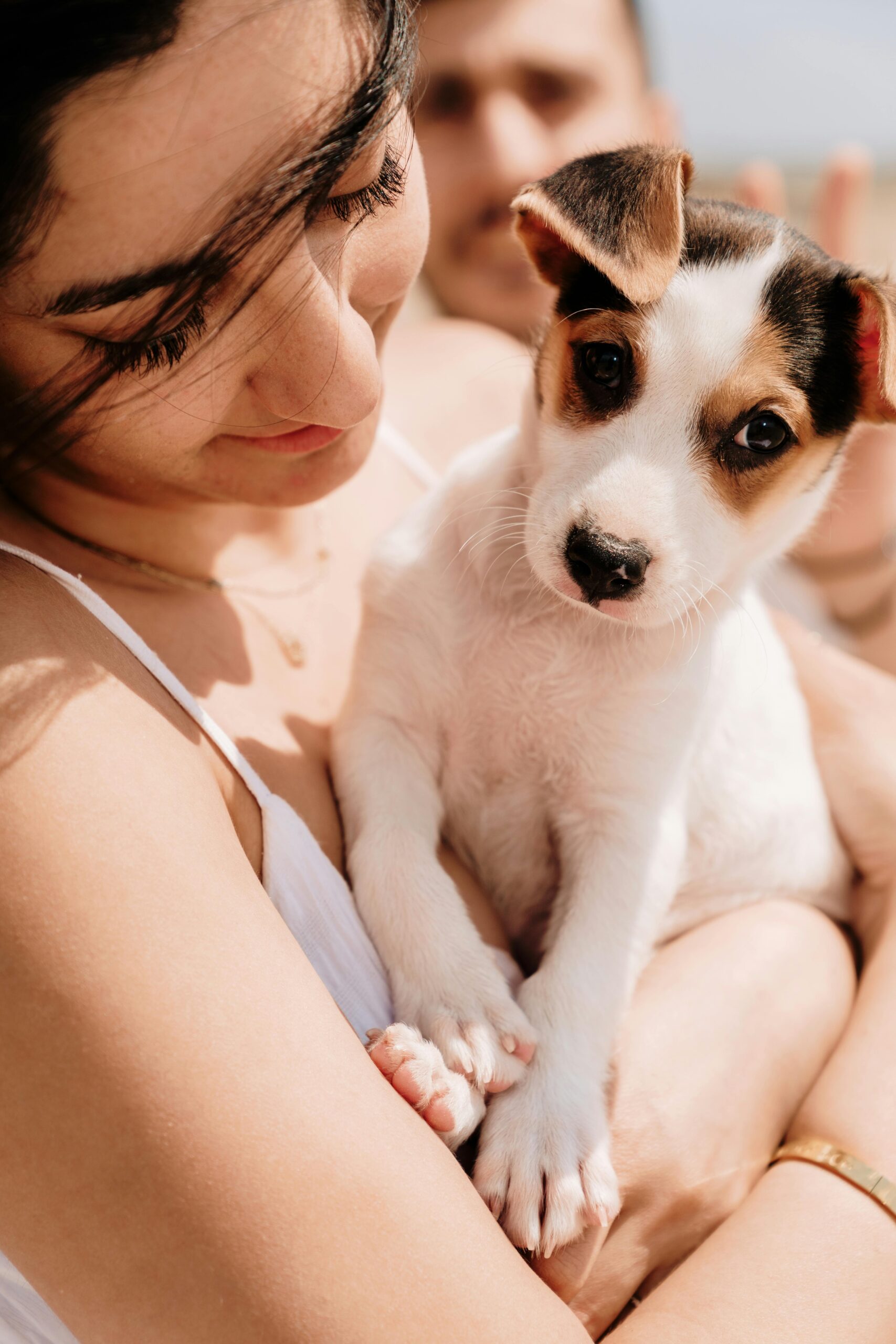 A woman lovingly holds a cute puppy under the sun, capturing a tender moment.